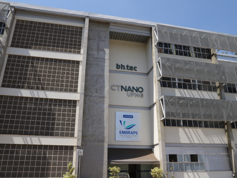 Fachada de edifício institucional com arquitetura moderna, identificado com as marcas bh.tec, CTNano UFMG e unidade EMBRAPII, sob céu azul, com estruturas metálicas nas laterais e entrada principal ao nível da rua.