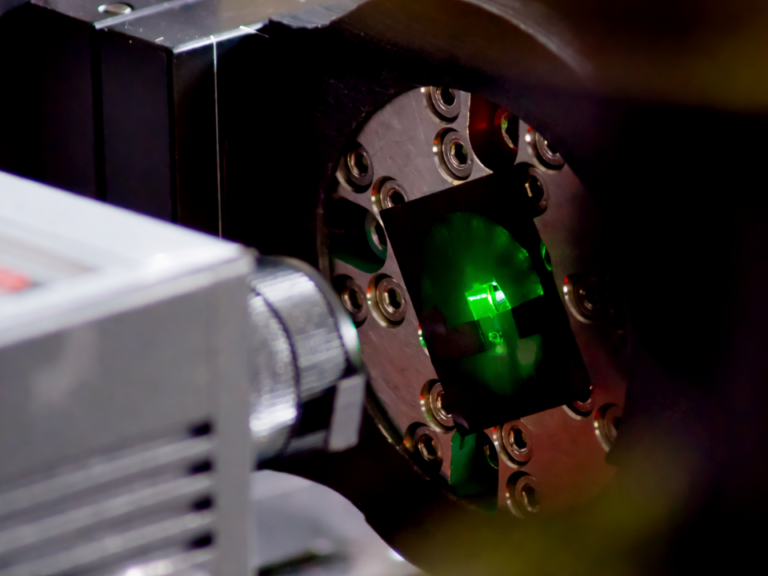 Equipamento de difração de raios X analisando amostra sólida com feixe incidindo sobre material cristalino.