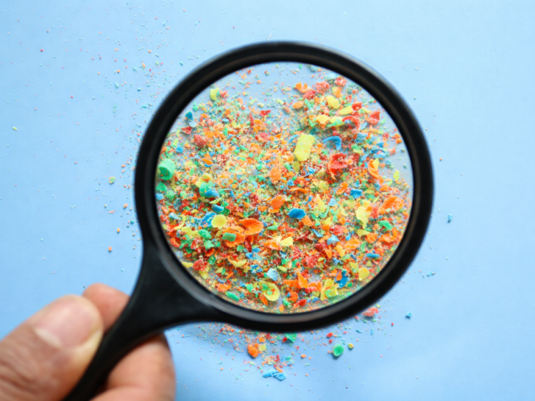 Microplásticos coloridos observados por meio de lupa, ilustrando os desafios da análise analítica e do controle de qualidade na detecção dessas partículas.