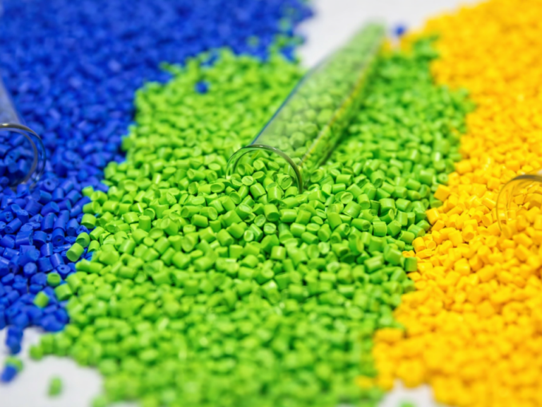 Pellets plásticos coloridos em azul, verde e amarelo dispostos em laboratório, representando matérias-primas poliméricas usadas na ciência dos materiais.