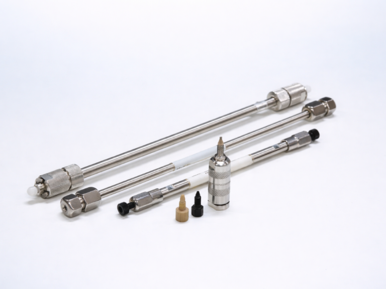 Colunas cromatográficas HPLC em aço inox com acessórios de conexão dispostas sobre fundo claro com leve tonalidade azul, em composição técnica de laboratório.