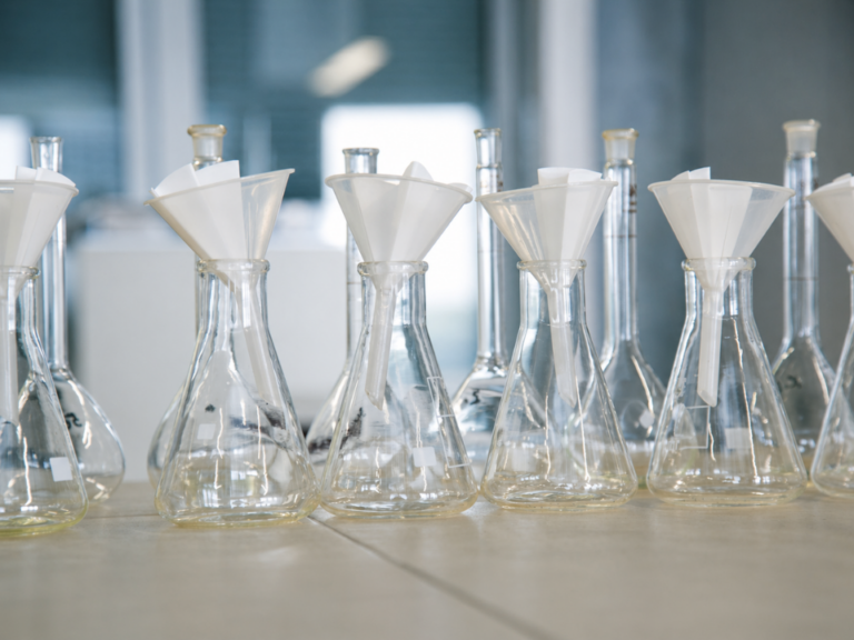 Laboratório analítico moderno com preparação de amostras avançada, mostrando frascos Erlenmeyer com funis e filtros em bancada limpa, ambiente controlado e iluminação fria, representando técnicas de microextração e uso de sorbentes seletivos para análises de alta precisão.