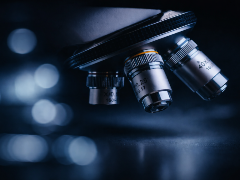 Objetivas de microscópio em close, com iluminação azul e foco seletivo, destacando lentes metálicas em ambiente laboratorial, representando análise microscópica e investigação científica.