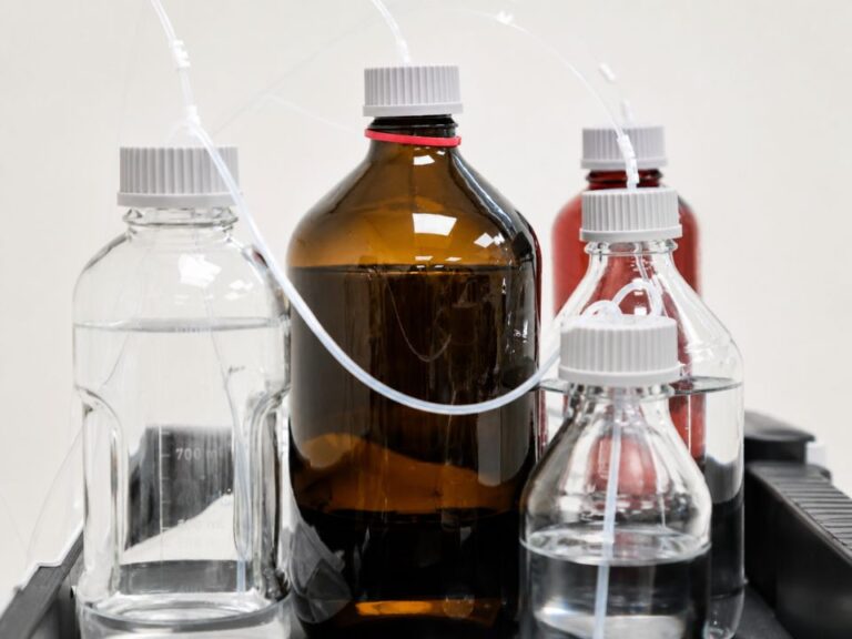 Frascos contendo fase móvel em HPLC conectados ao sistema cromatográfico, representando o impacto da qualidade dos solventes, estabilidade química e preparo adequado no desempenho analítico.